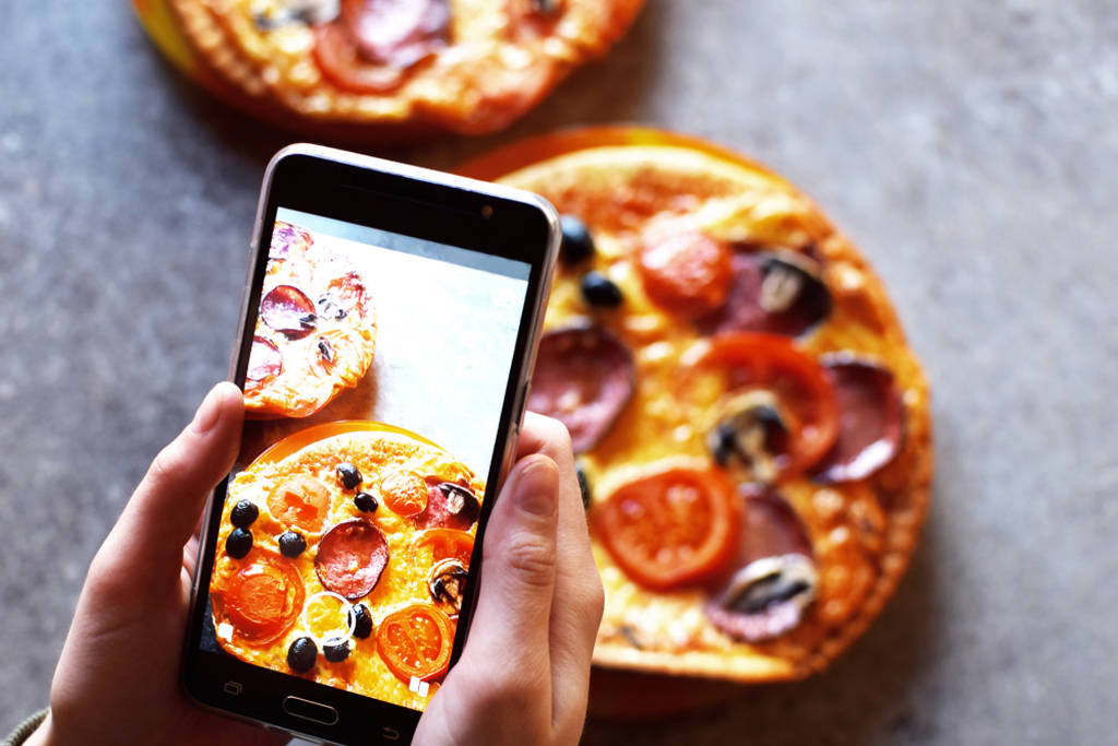 Pessoa fotografando duas mini pizza usando a câmera do smartphone, simbolizando como calibrar cores da tela do celular