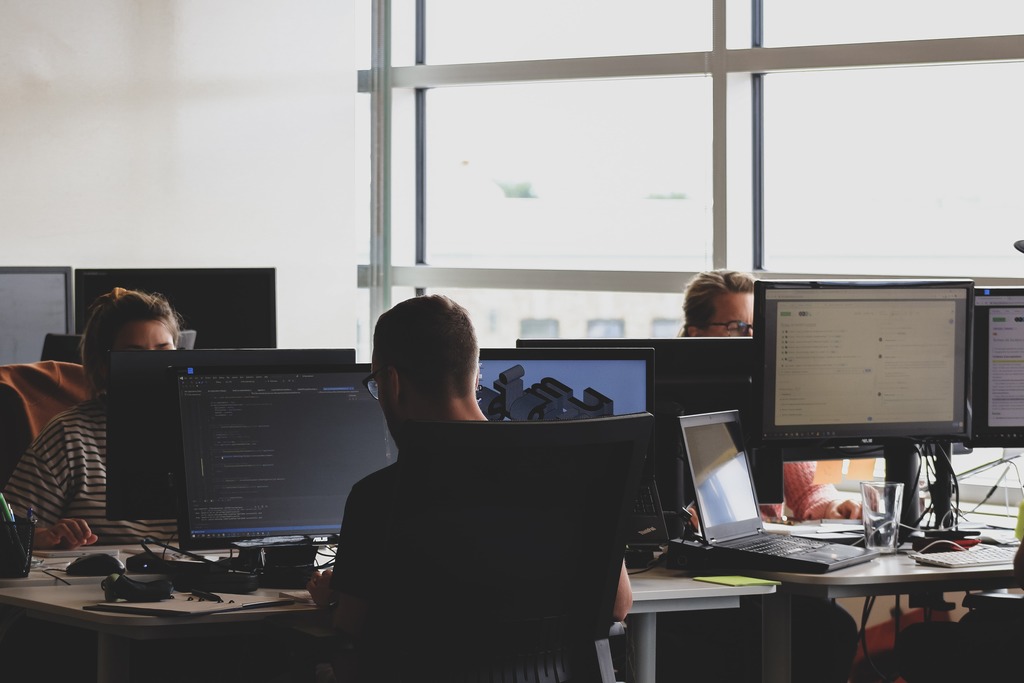 Três pessoas em ambiente corporativo (escritório com nichos de computador), cada uma usando seu monitor LCD industrial