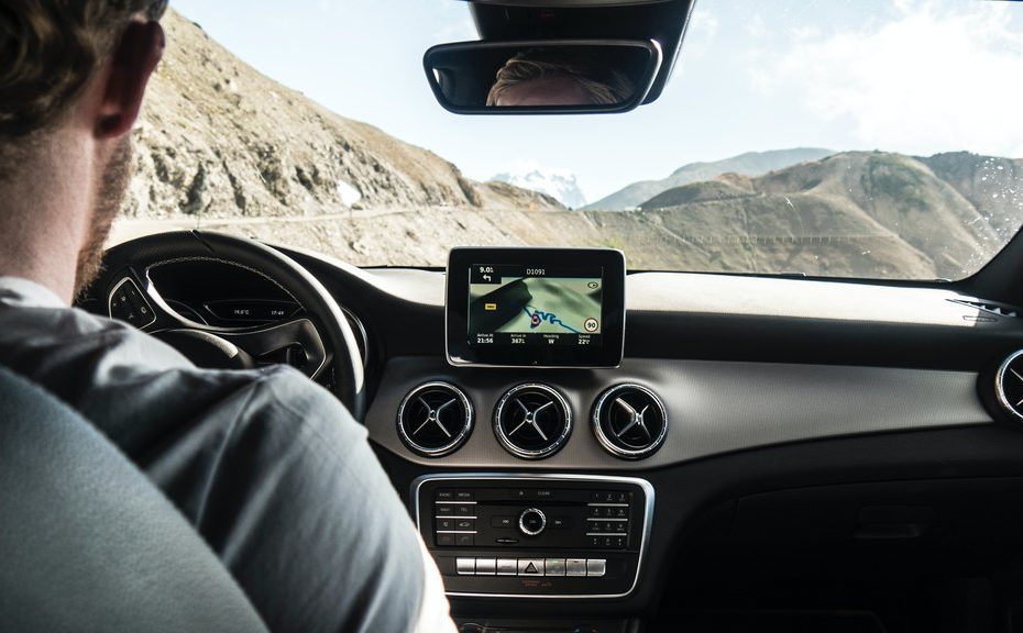 Interface multimidia, no caso um monitor ligado com GPS no painel de um carro que está andando numa estrada de asfalto em região montanhosa