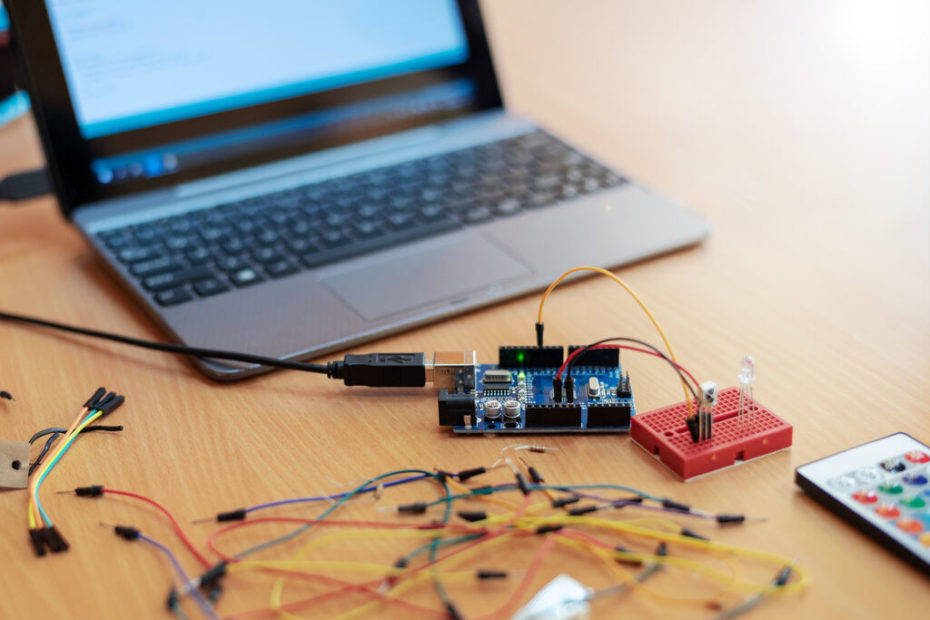 Notebook com tela ligada, simbolizando o Arduino IDE, conectado ao hardware Arduino com cabos sobre a mesa