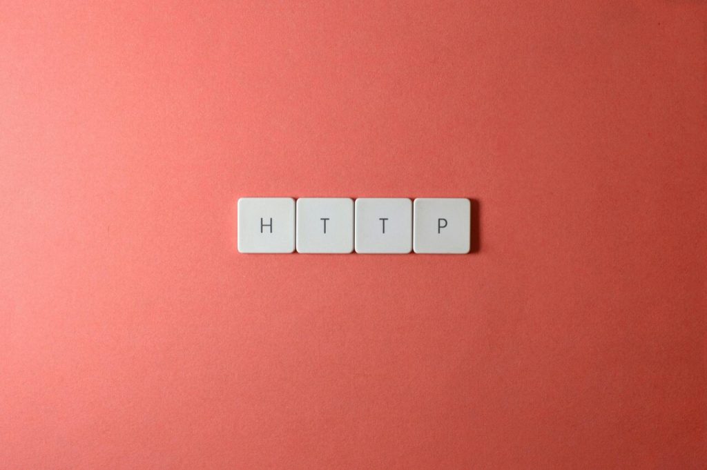  Quatro teclas brancas de teclado com as letras "HTTP" em preto estão alinhadas horizontalmente sobre um fundo vermelho-alaranjado. A imagem representa o protocolo HTTP, um dos principais protocolos de comunicação utilizados na transferência de páginas web na internet.